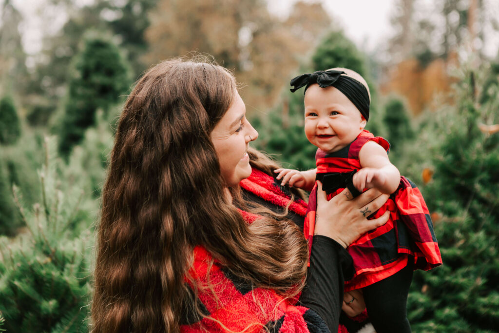 A mother and infant daughter smiling at each other in a Christmas tree farm Salem, OR