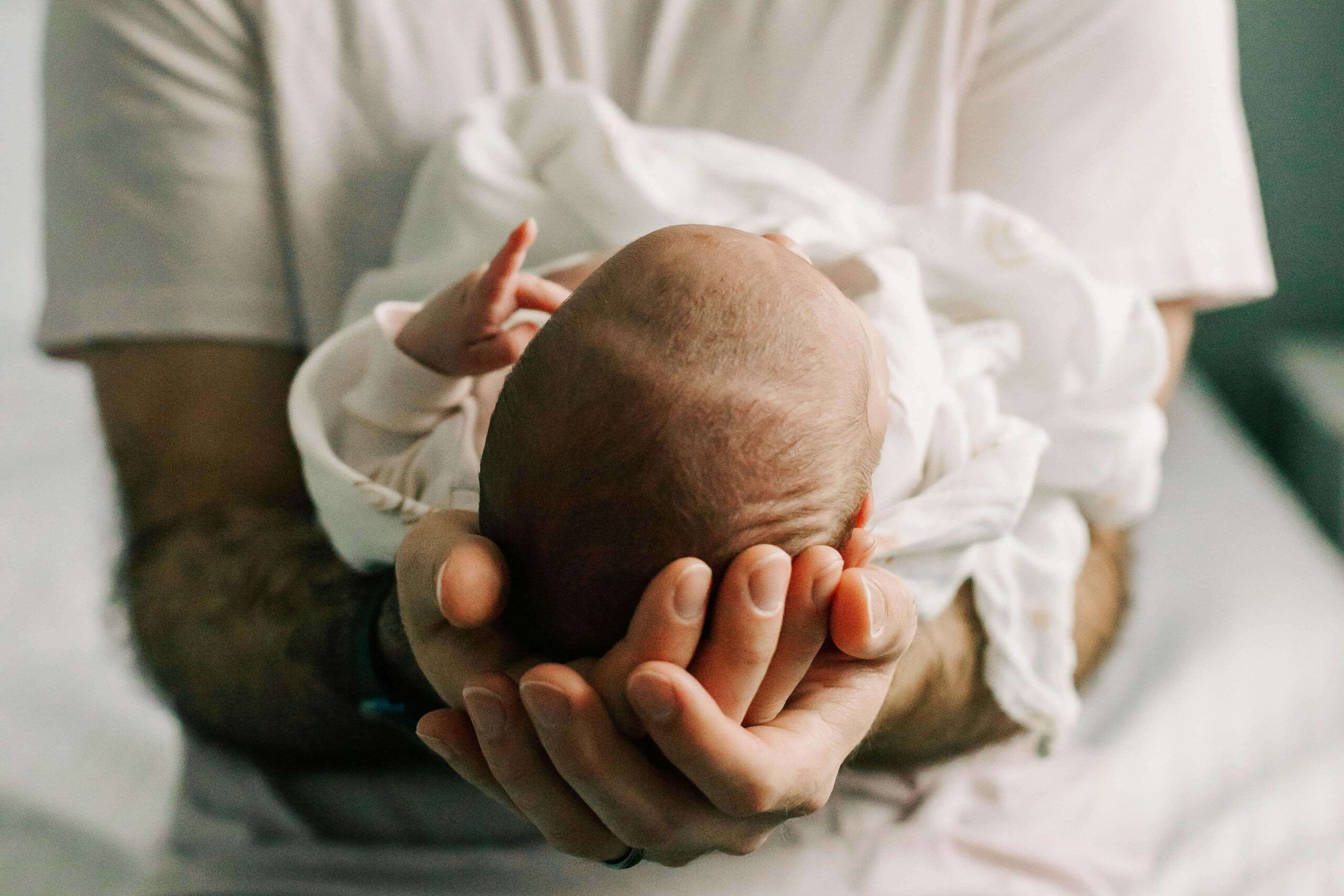 A father holds his new infant in his arms, cradling the baby's head in his hands