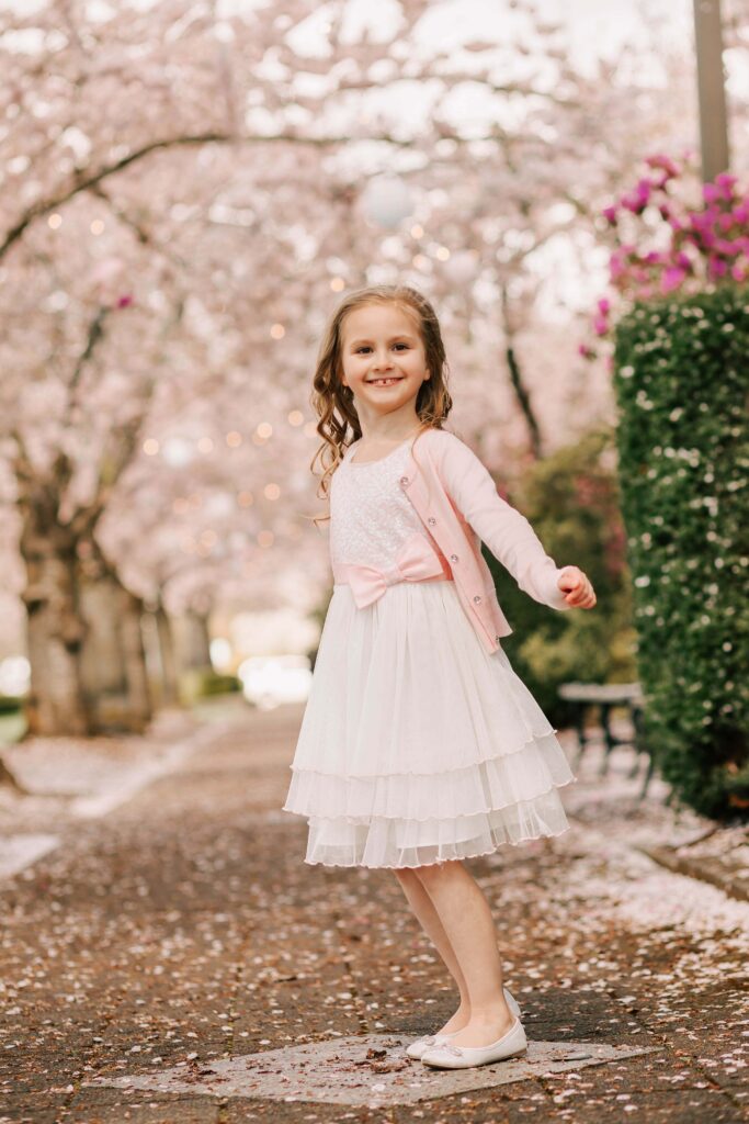 A young girl in a white dress stands in the cherry blossoms at the capitol in Salem, OR