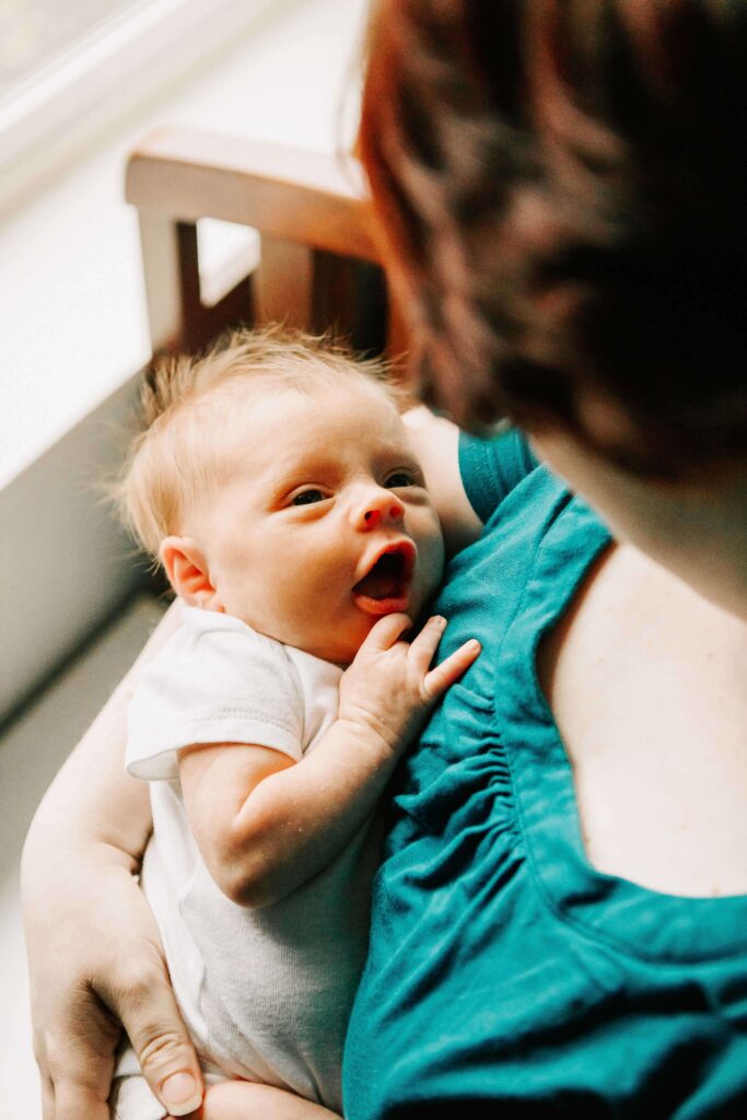 A mother in a teal shirt holds her baby and the baby looks up at her smiling