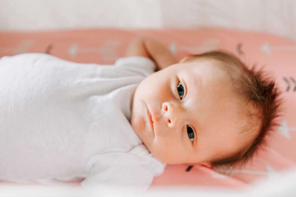 A newborn baby in a white onesie lies on a pink blanket