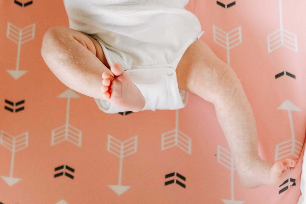 A baby in white onesie kicks her legs