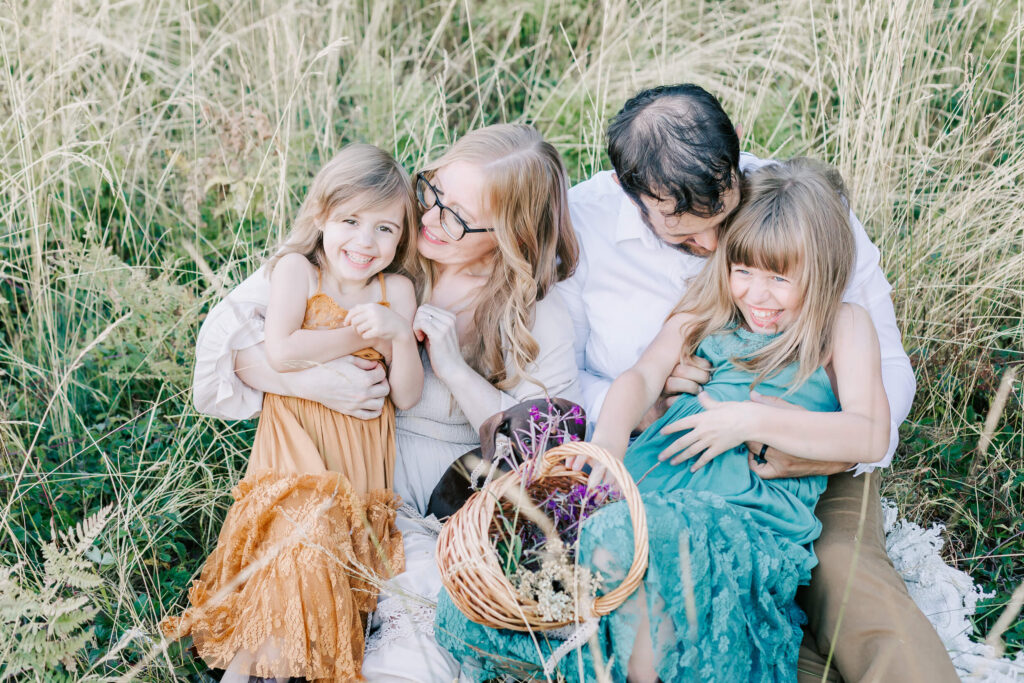 A mother, father, and their 2 daughters sit together laughing