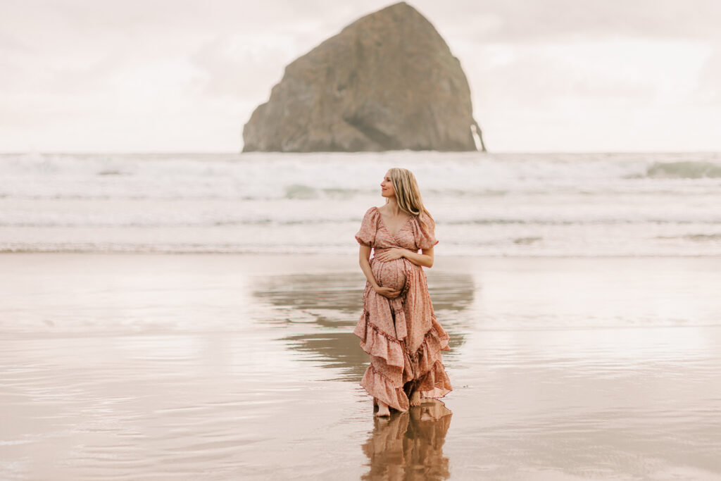 A pregnant mother poses for a photo in front of haystack rock at Cape Kiwanda on the Oregon coast.