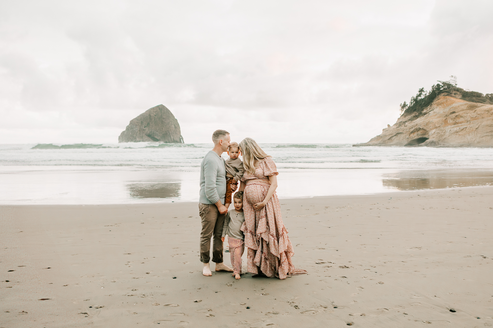 A family huddles together on the Oregon Coast in front of haystack rock at Cape Kiwanda State Park