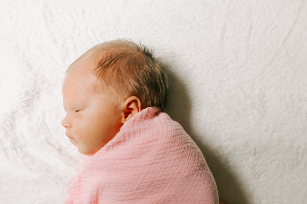 A newborn baby wrapped in a pink blanket lays on a bed