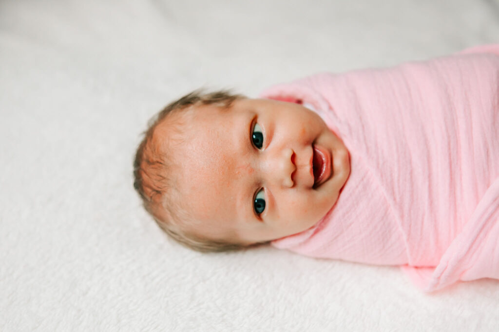 A newborn baby swaddled in pink smiles 