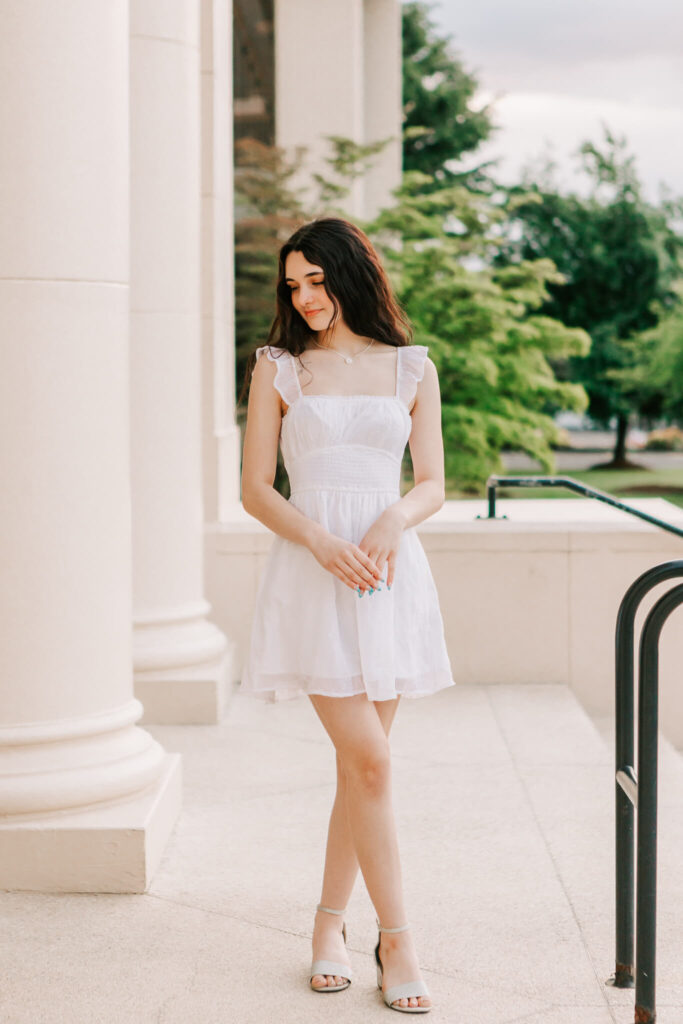 A high school senior in a white dress poses downtown albany for senior portraits