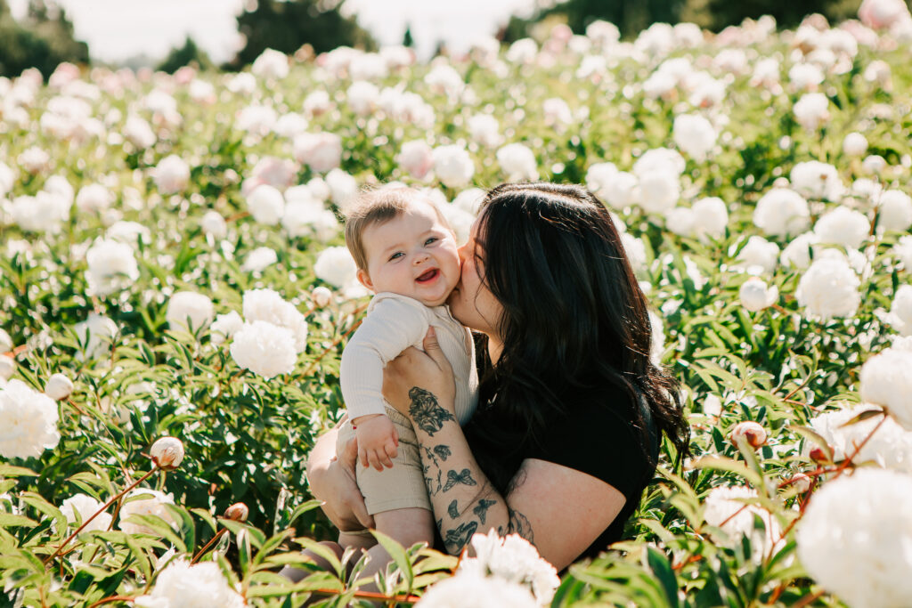 A mom kisses her baby surrounded by peonies at Adleman Peony Gardens in Salem, OR
