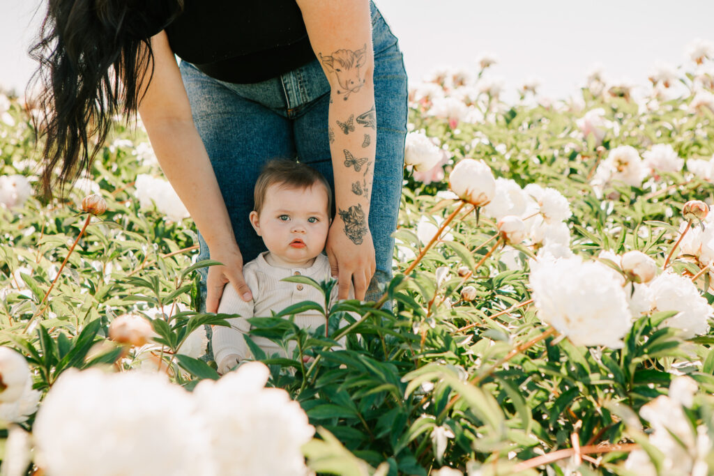 Baby stands in the peony garden with help from his mother at Adelman Peony Garden Mini Sessions 