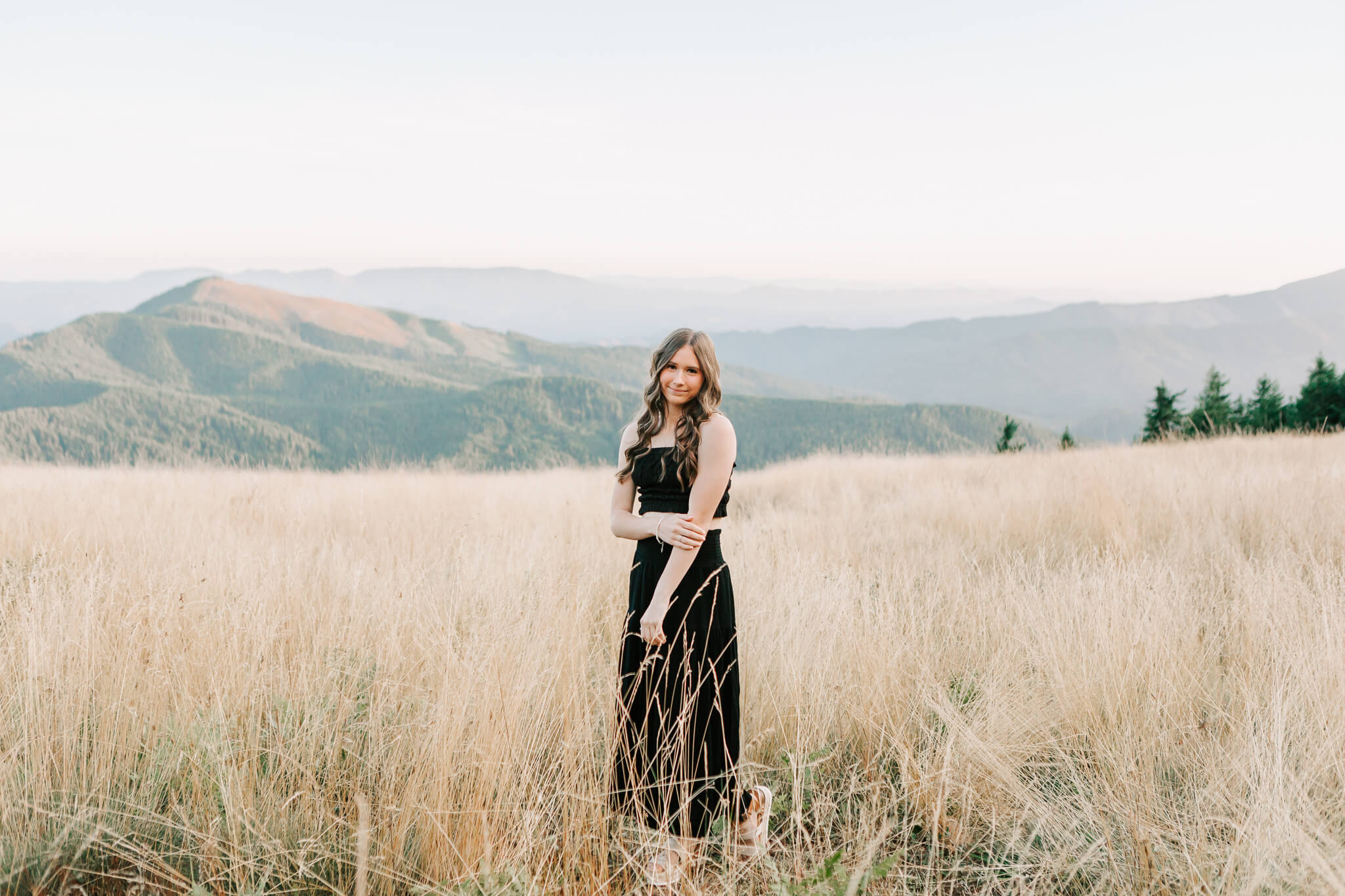 High school senior standing in a black dress at Mary's Peak. Senior photo by Jen White Photography