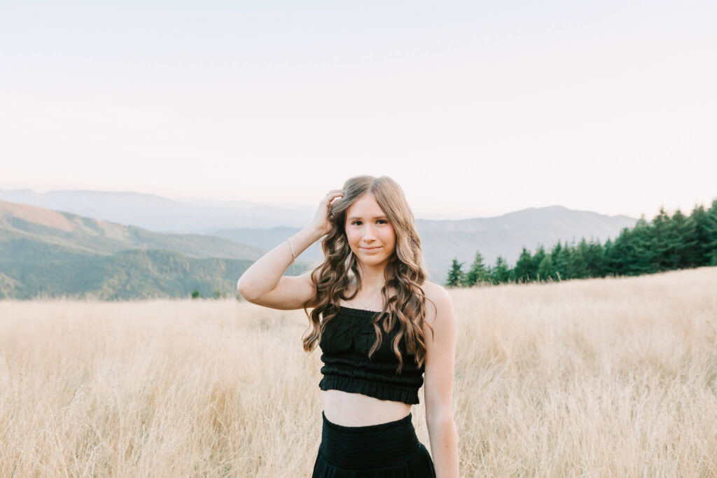 A woman stands in a mountain field in a black dress 