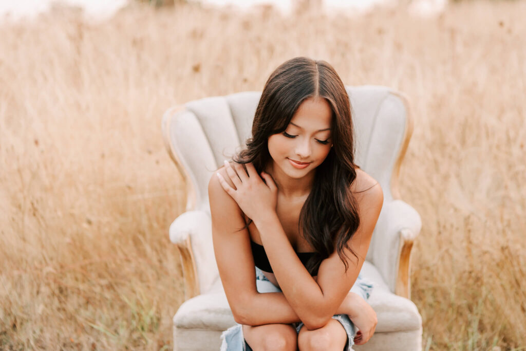 Senior girl in a chair in a field looking down. Photo by Jen White Photography Albany, Oregon