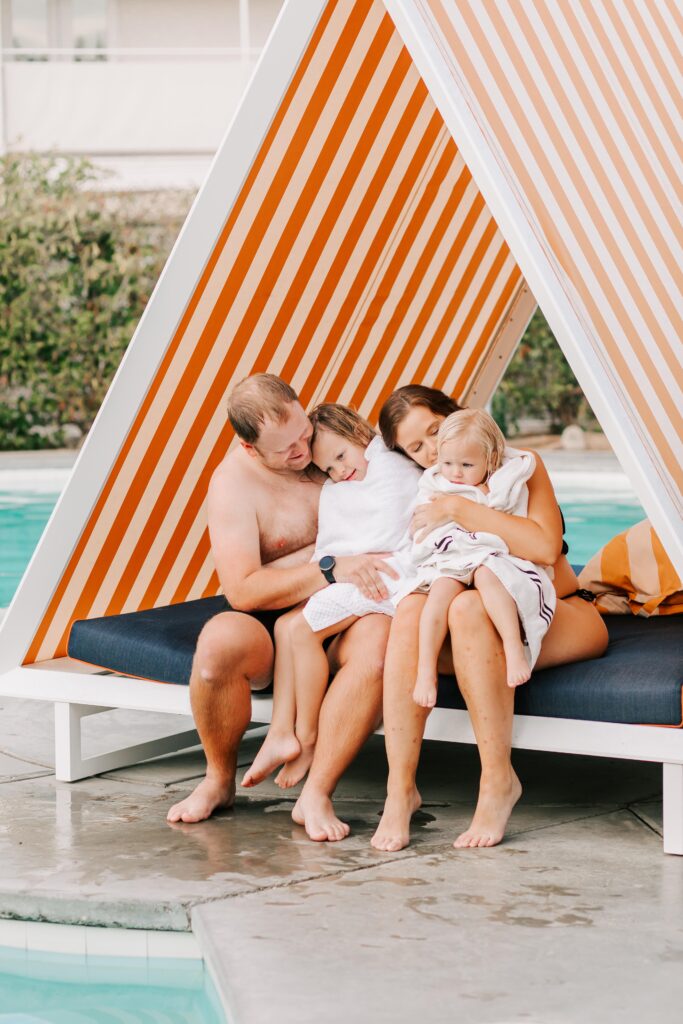 A mother and father wrap their 2 young daughters in a towel after swimming