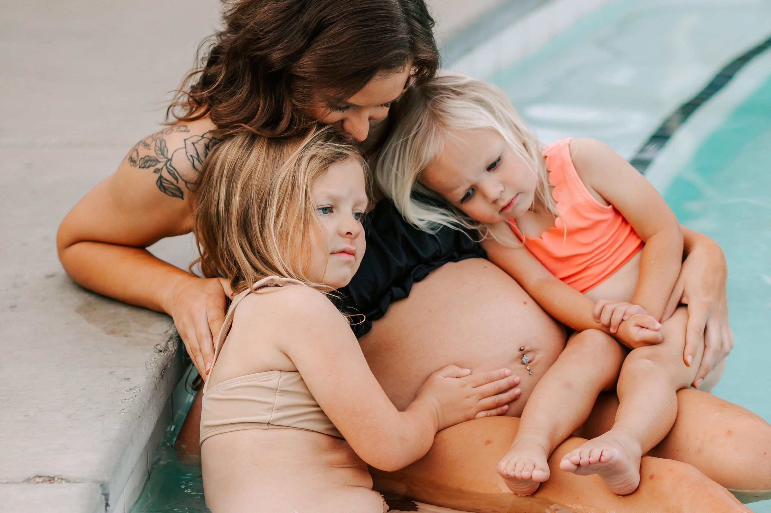 A mom sits in a pool with her 2 young daughters