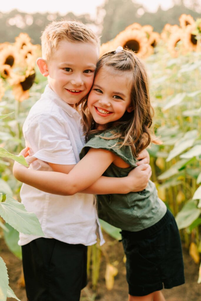 A brother and sister hug in a sunflower field