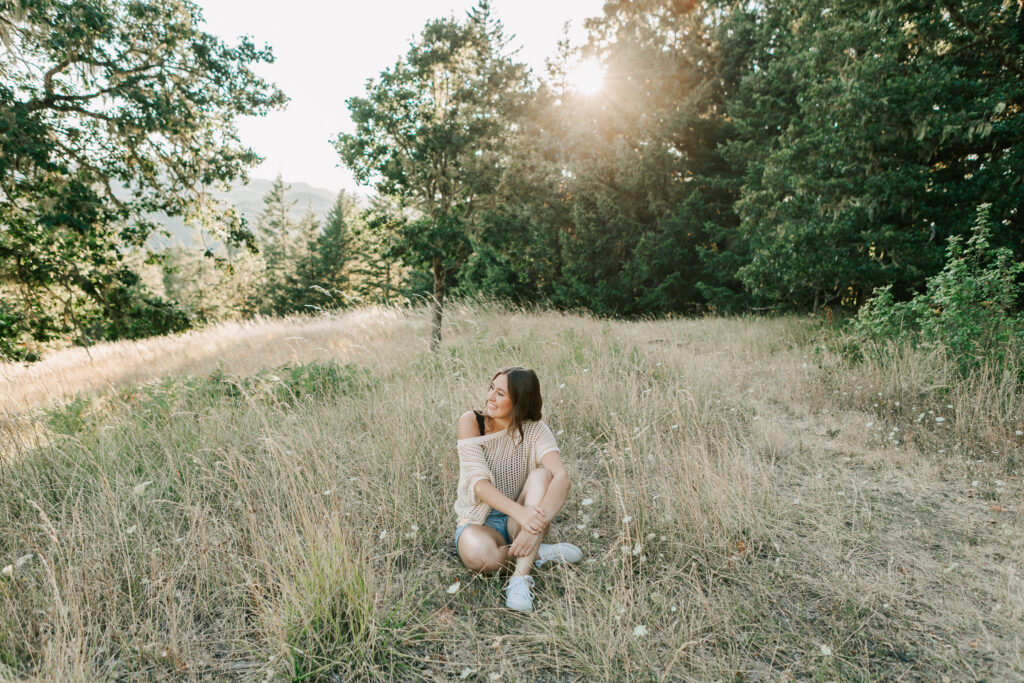 A high school senior sits on a mountain posing for senior portraits in a sweater and shorts