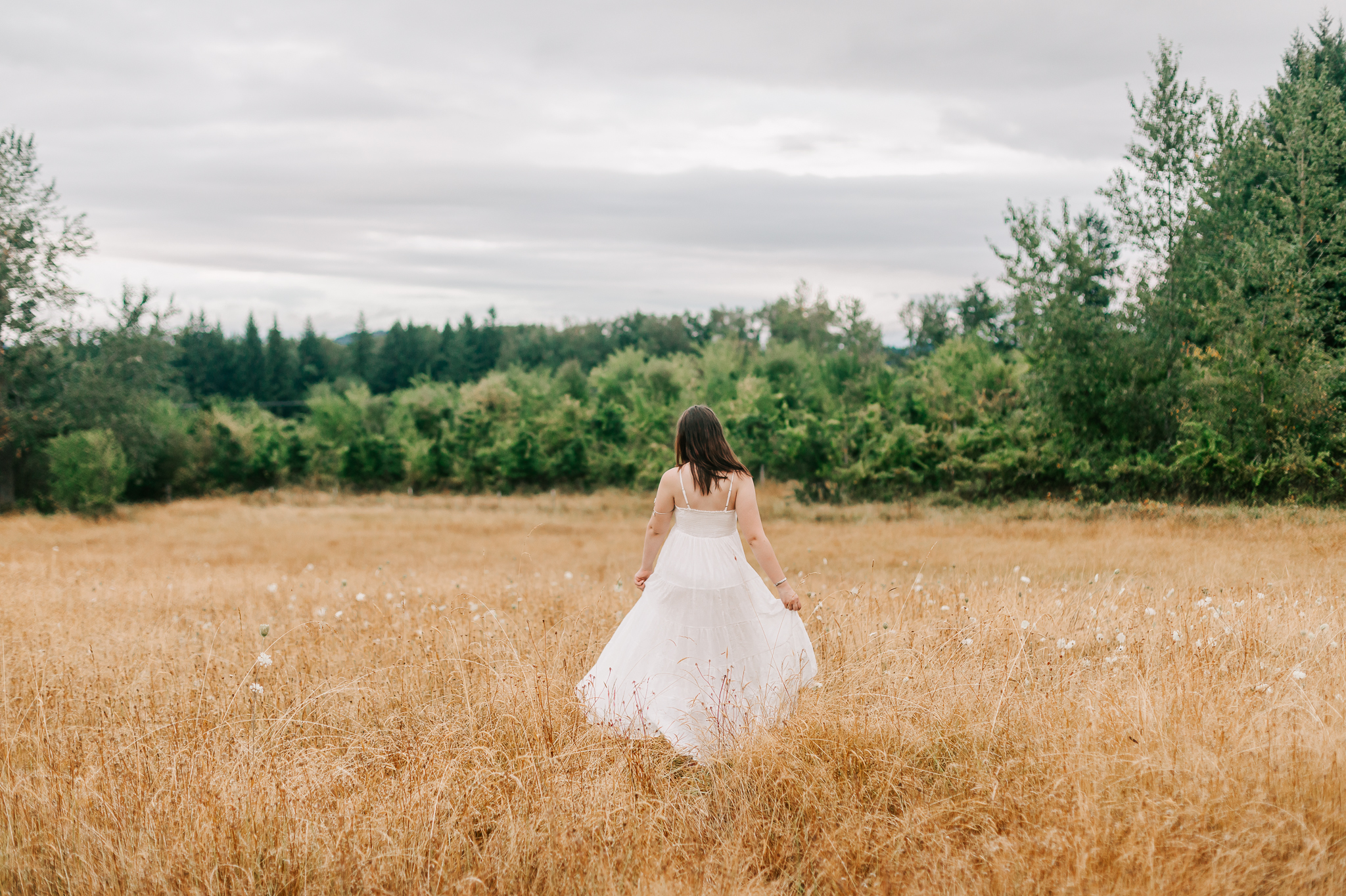 High school senior walks through field in white flowy dress