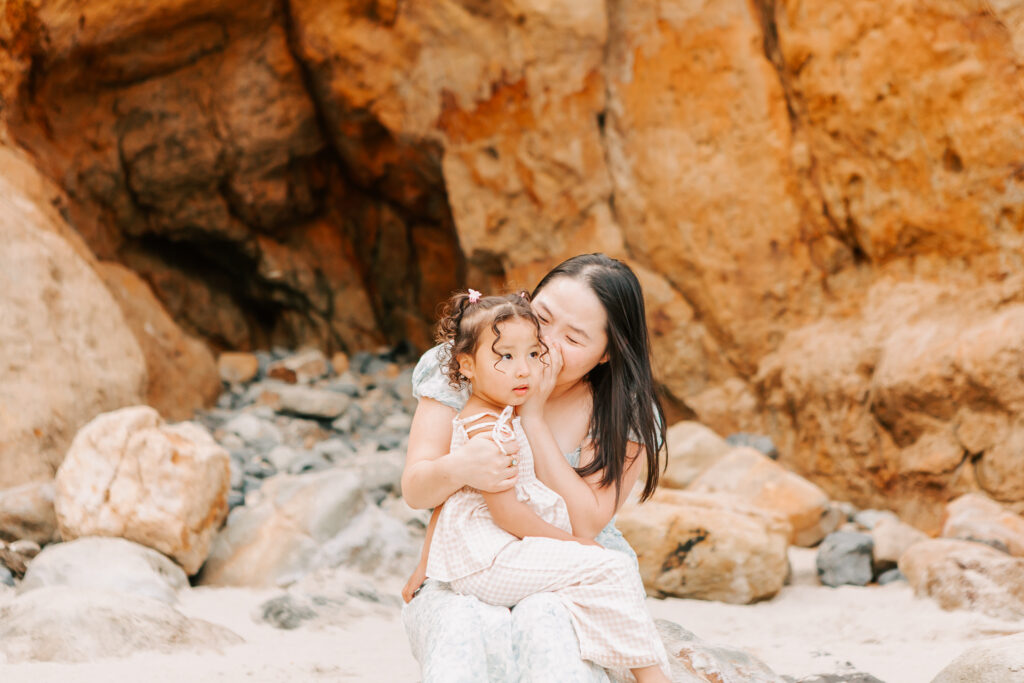 A mom whispers in her preschool daughter's ear at Cape Kiwanda on the Oregon Coast