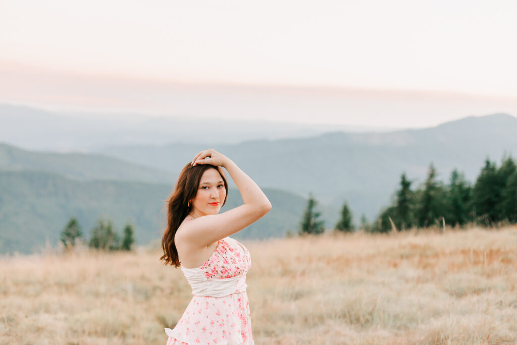 Senior girl wearing a soft-colored dress standing in a grassy field with Oregon mountain views during golden hour. Photo is by Jen White Photography of Albany Oregon