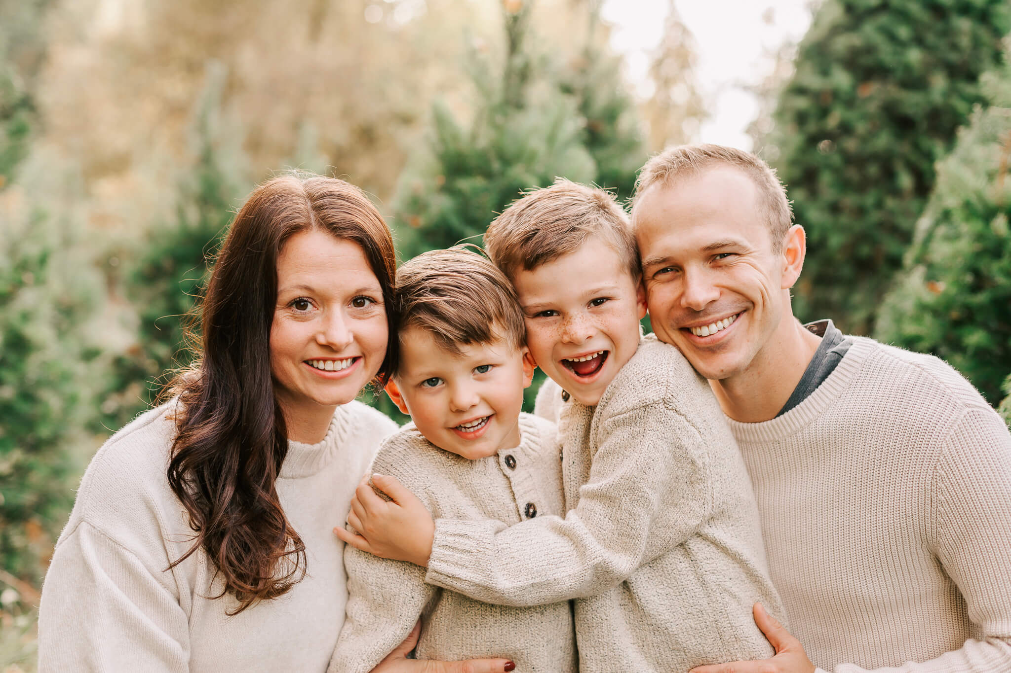 A family poses for family portraits at a Christmas tree farm in Salem Oregon with Jen White Photography. They are wearing jeans and cream sweaters.