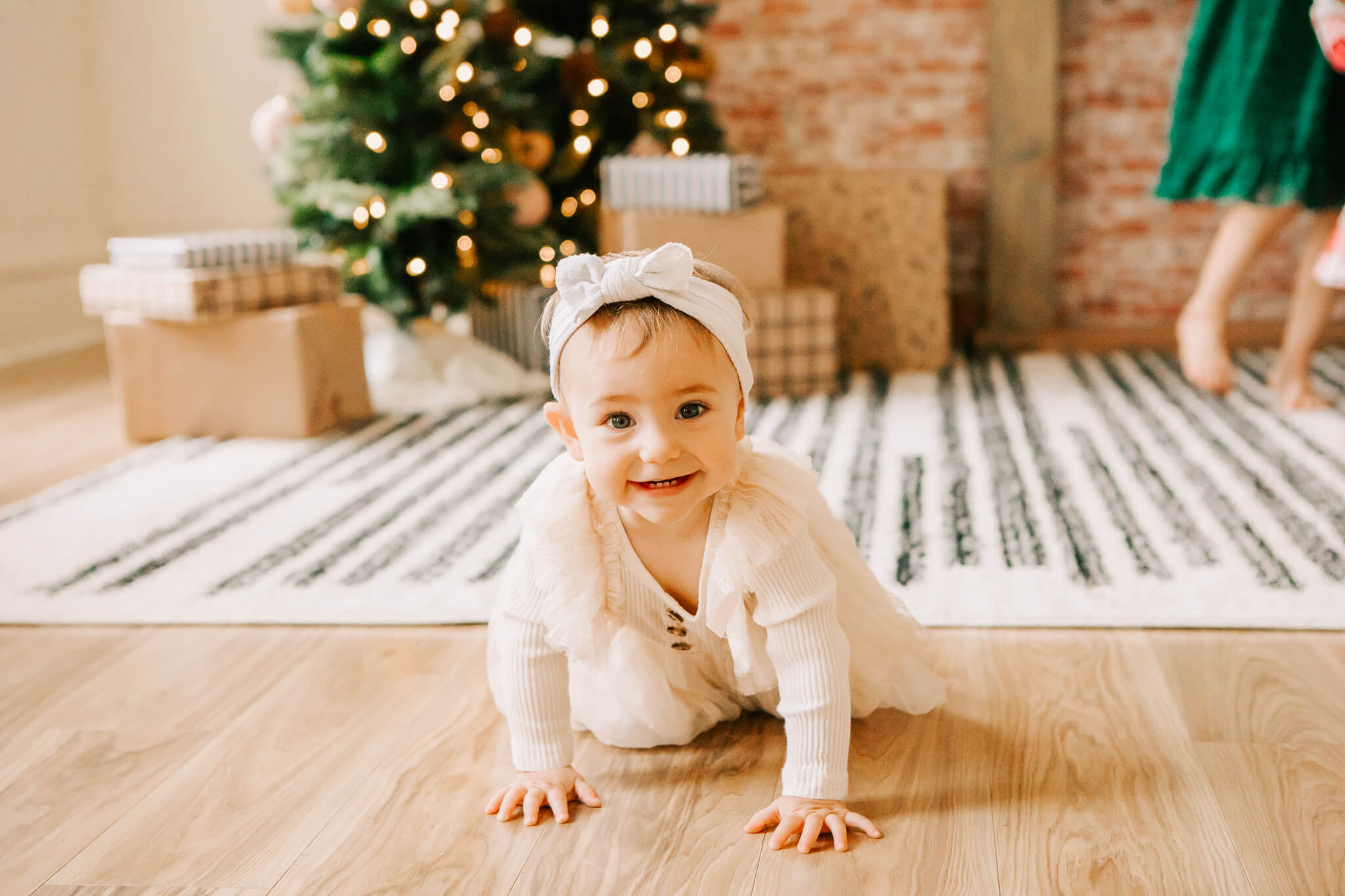 Baby crawling and smiling with lighted Christmas tree and wrapped gifts in the background during Salem Christmas studio minis with Jen White Photography of Albany Oregon