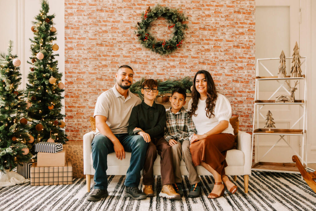 Family smiling together during studio Christmas mini session in Salem OR with small decorated tree and cozy holiday setup