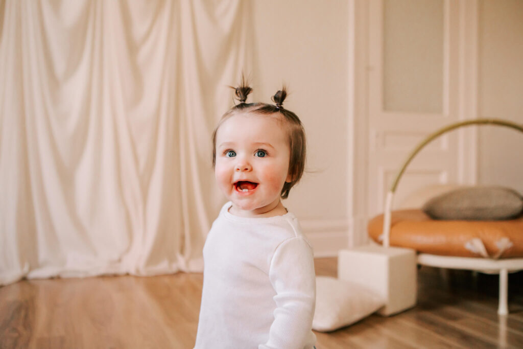 Toddler girl with high pigtails looks at camera and smiles