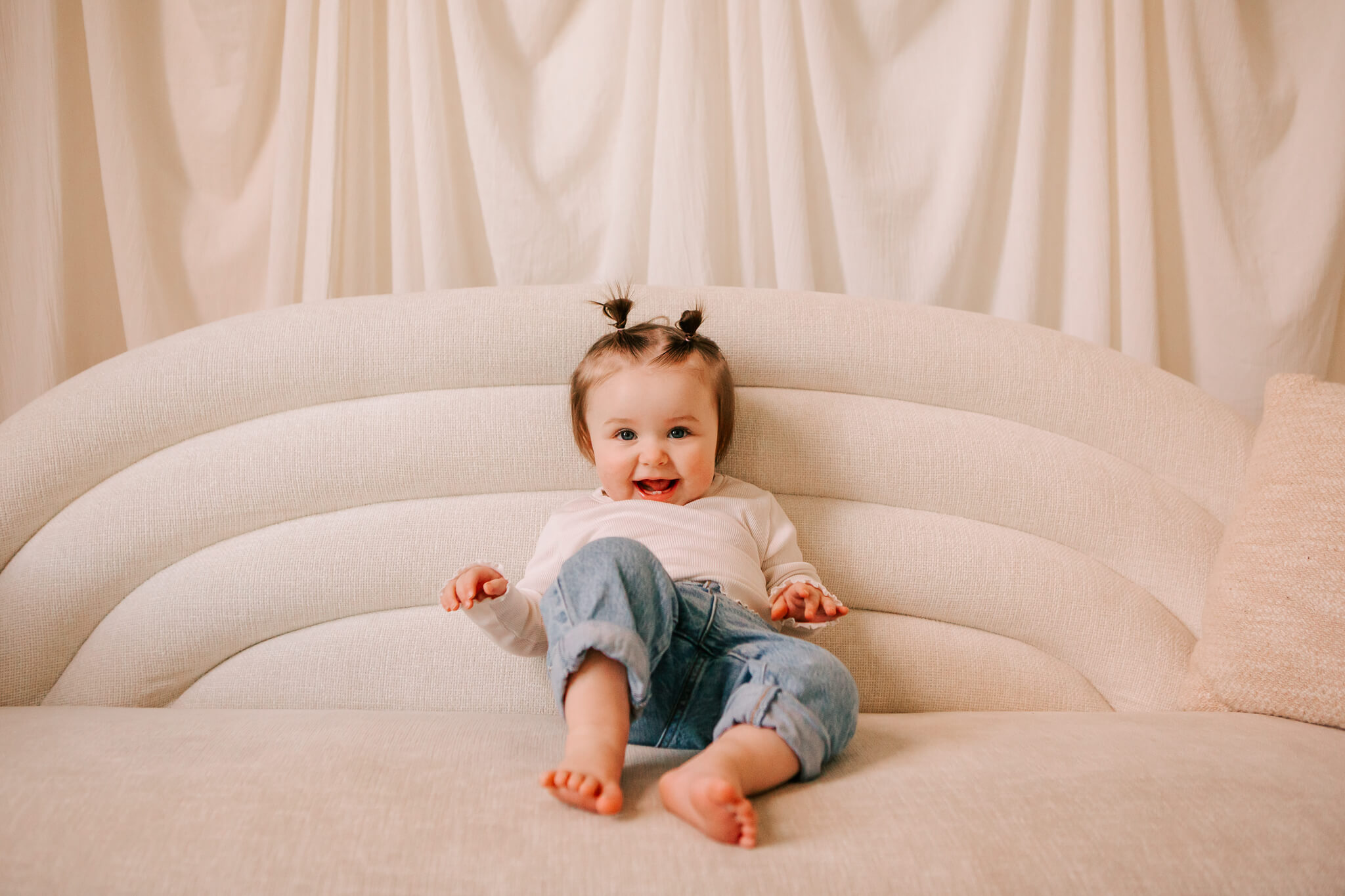 Toddler girl with pigtails in jeans and a white shirt laughs at the camera