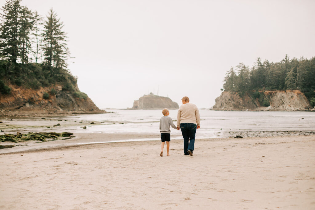 A mom and her young son walk on the beach  holding hands at Sunset Bay State Park in North Bend Oregon