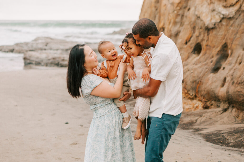 A family plays on the Oregon Coast. Mom and dad are holding their son and daughter at Cape Kiwanda State Park
