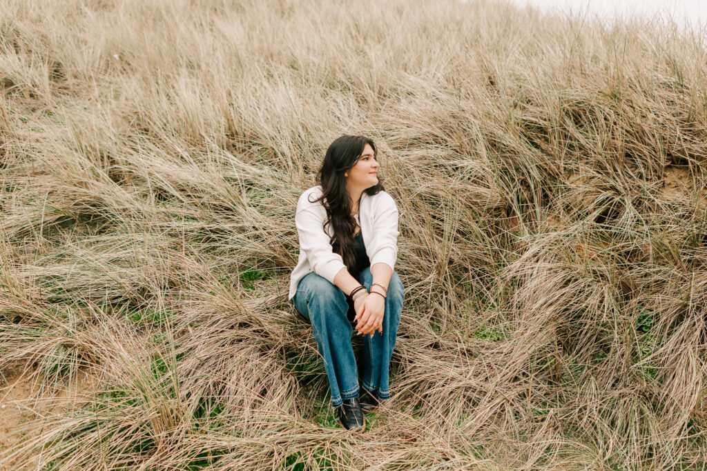 A young woman sits in the sea grass during Oregon Coast Senior Photos