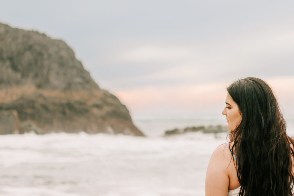 A young woman stands on the beach facing the ocean