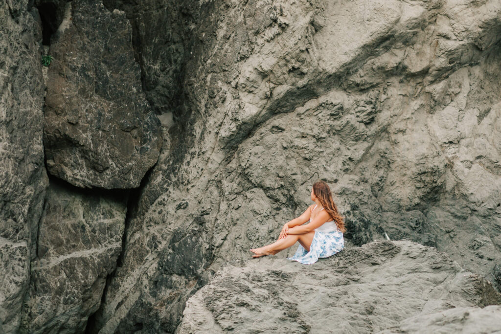 A young woman sits on the rocks at the beach