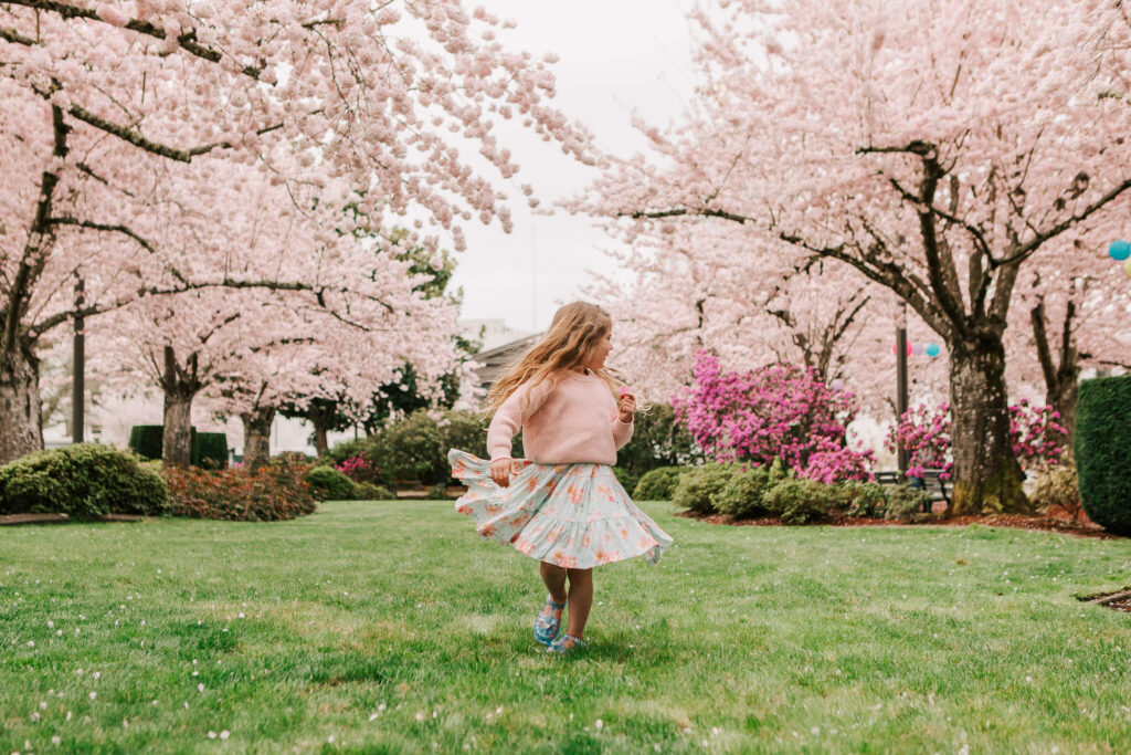 A young girl in a skirt runs in the grass under the cherry trees at Salem, Or Capitol during cherry blossom days at the capitol