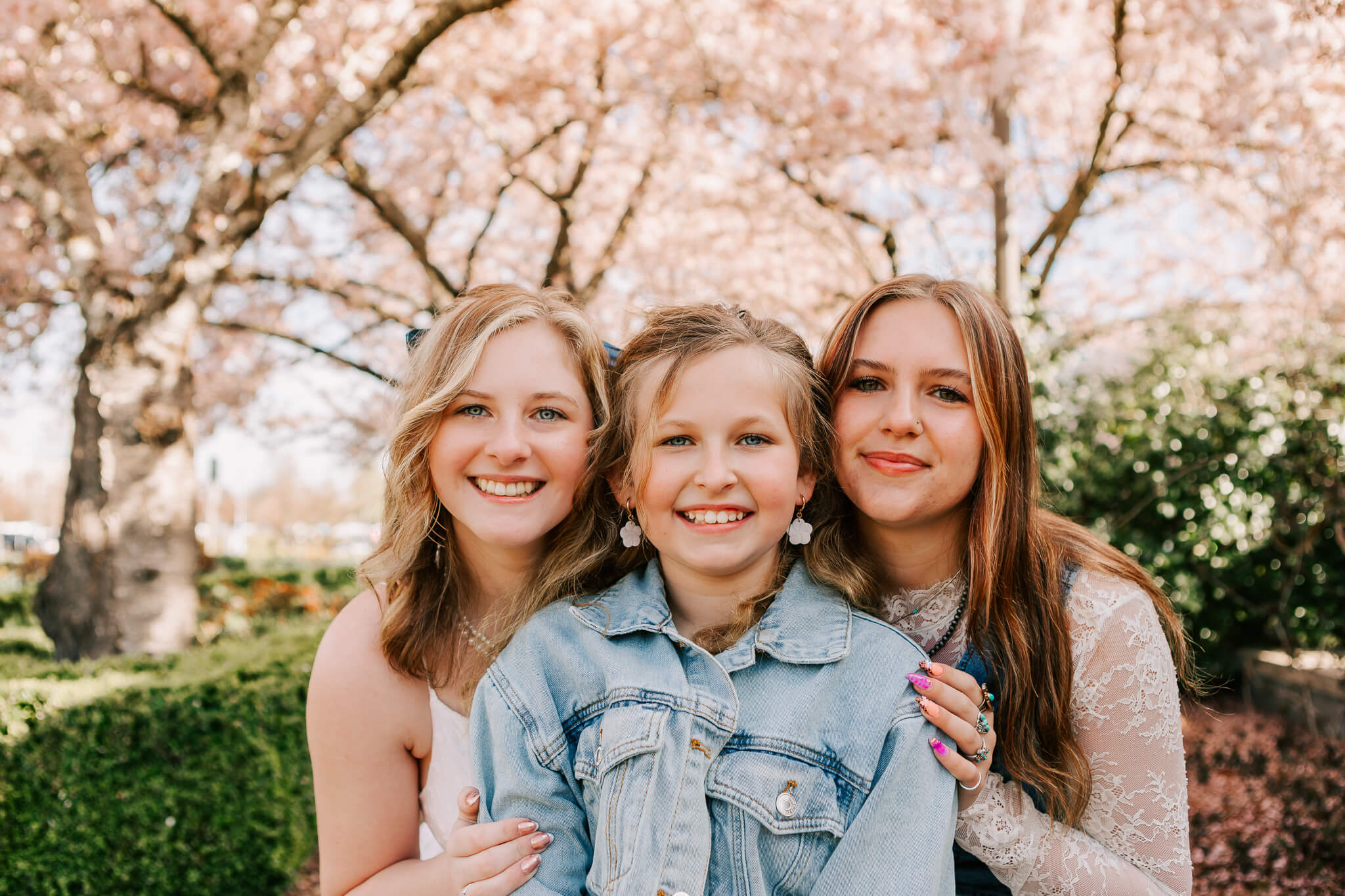 3 sisters pose in front of the cherry trees in Salem Oregon at Spring mini family photo session with Jen White Photography