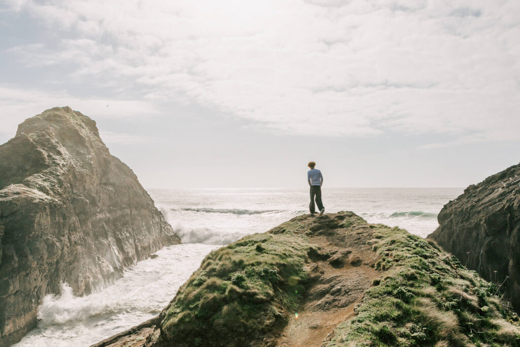Young man stands on a grassy cliff looking out over the ocean