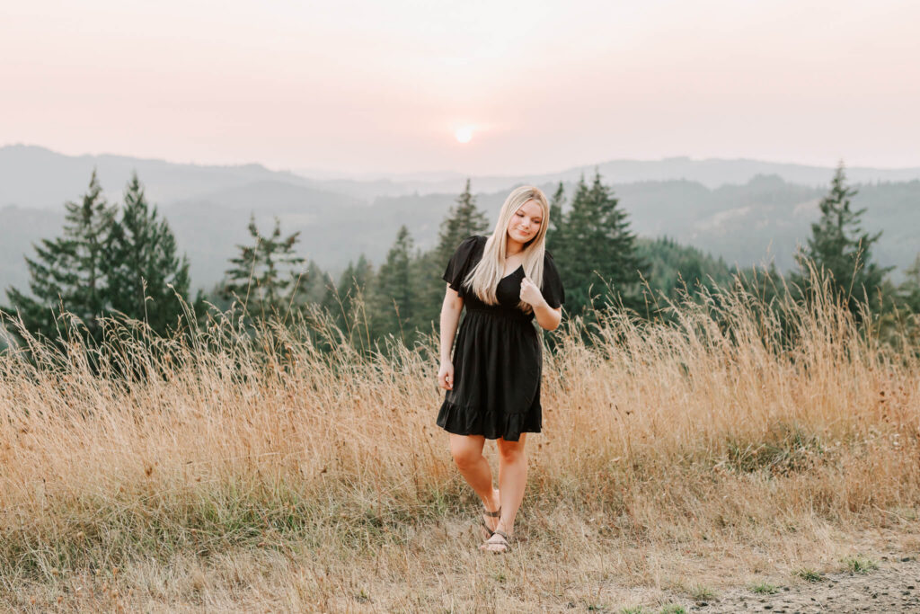 senior girl poses for senior photos with jen white photography in a golden field with trees in the background