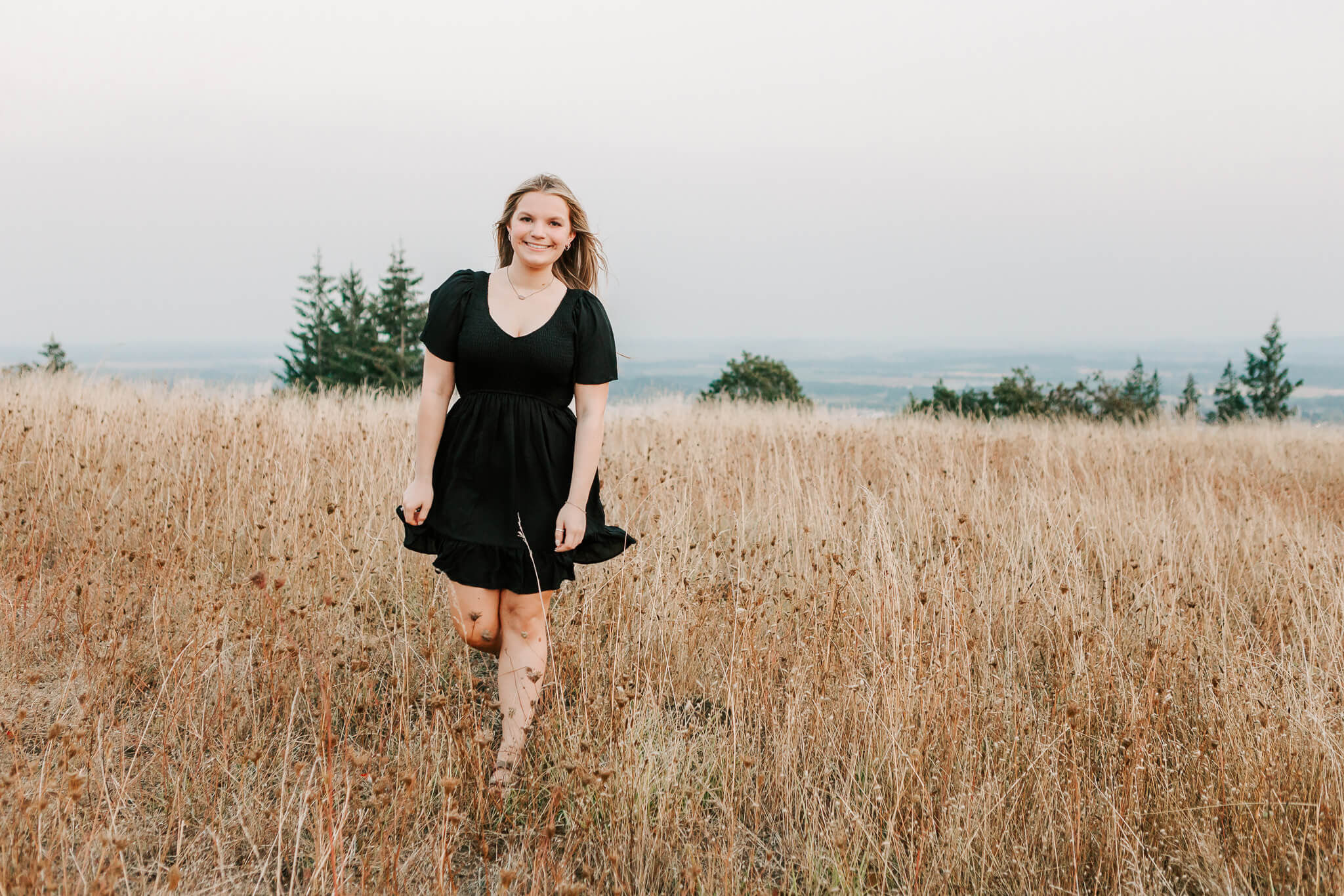 High school senior in black dress walking through a golden grassy field