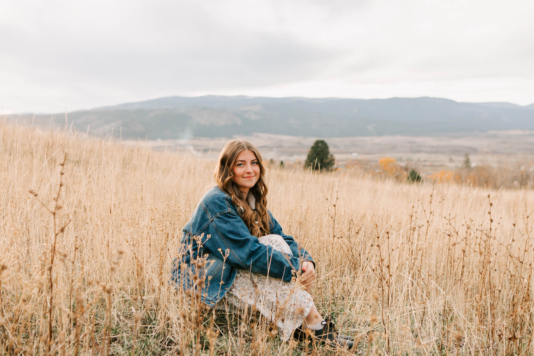 high school senior girl sits in tall grass holding her knees while posing for senior portraits with Jen White Photography